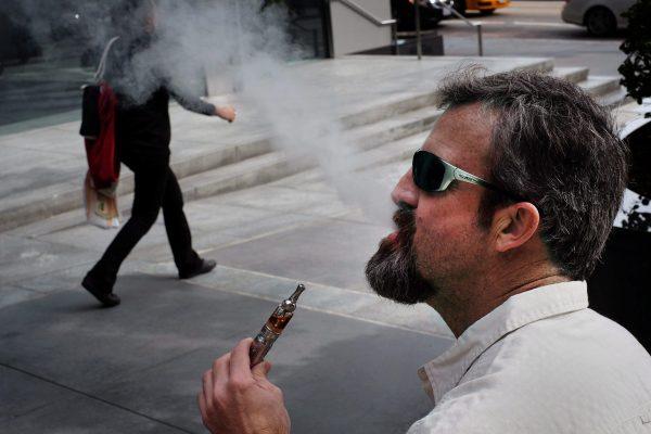 A man smokes an electronic cigarette in the street. As “vaping” grows in popularity, a parliamentary report released is recommending that the government establish new legislation for regulating e-cigarettes. (AP Photo/Richard Vogel)