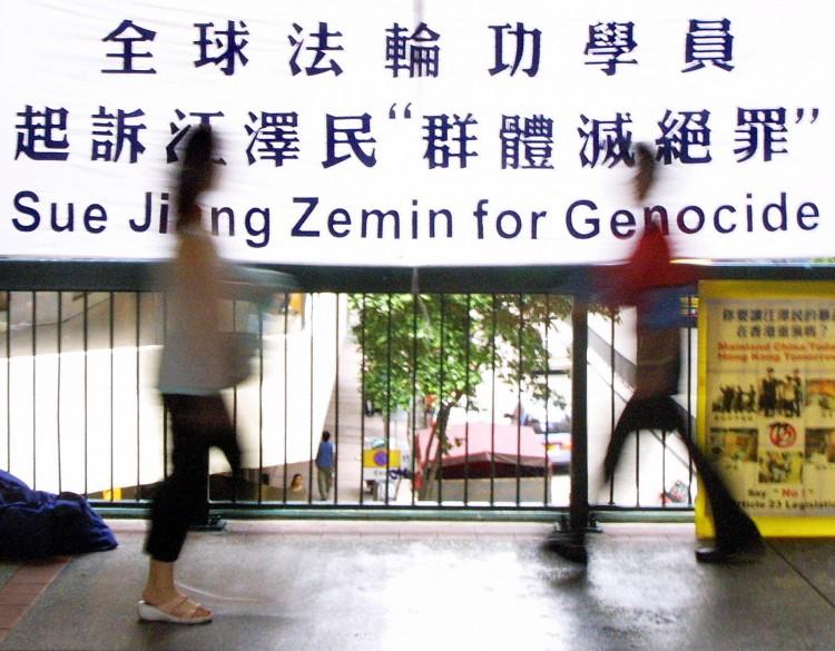 Residents walk past a protest banner supporting a lawsuit filed in Brussels against Chinese Communist Party head Jiang Zemin for genocide, on Aug. 30, 2003, in Hong Kong. (Laurent Fievet/AFP/Getty Images)