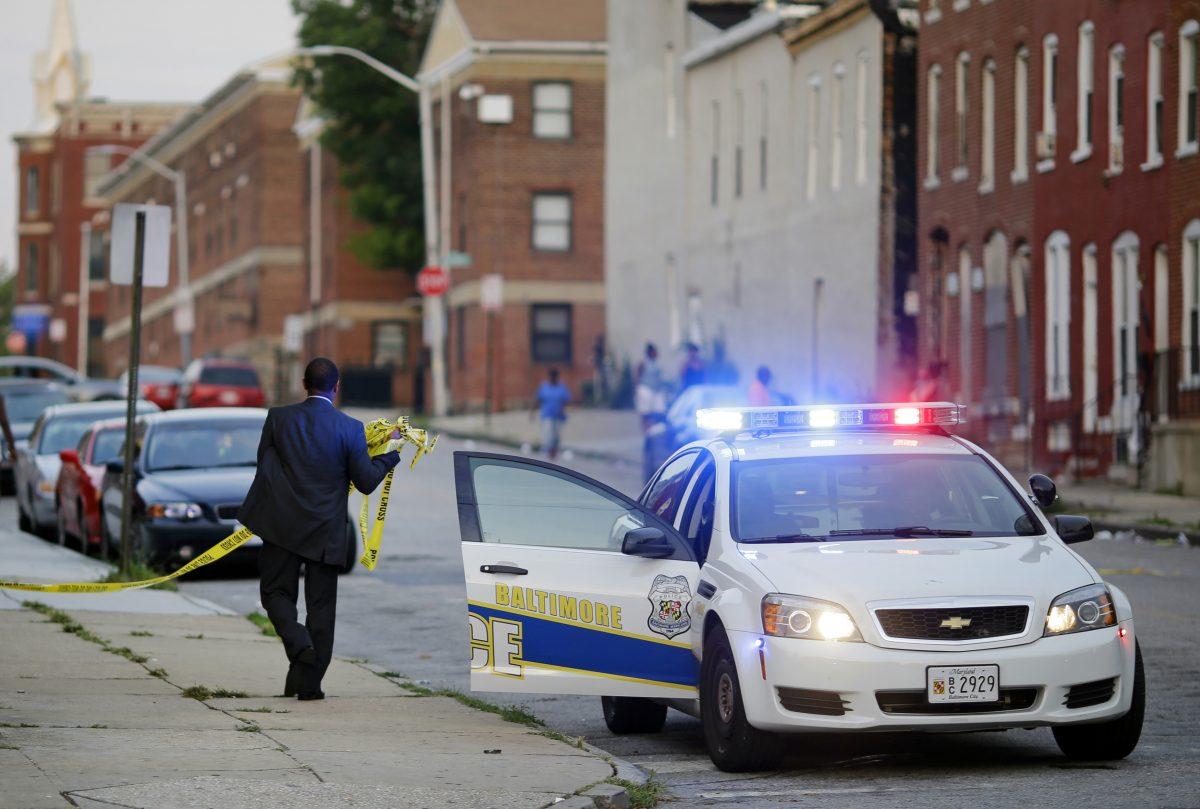 A member of the Baltimore Police Department removes crime scene tape on July 30, 2015, from a corner where a victim of a shooting was discovered in Baltimore. (Patrick Semansky/AP Photo)