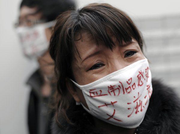 A woman, whose son was infected with HIV, wears a face mask bearing the words "Blood products infect us with AIDS," as she cries during an AIDS awareness event at Beijing's south railway station, on Dec. 1, 2009. (Andy Wong/AP Photo)