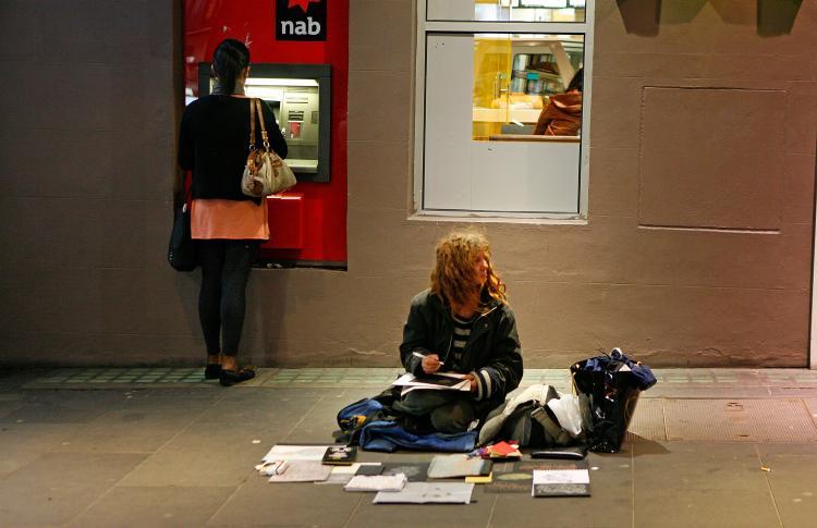 A woman sits on the pavement as a woman behind her withdraws money from an ATM machine in Melbourne, Australia on Aug. 31, 2009. (Scott Barbour/Getty Images)