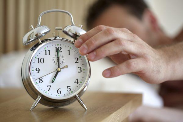 Man lying in bed turning off an alarm clock in the morning at 7am