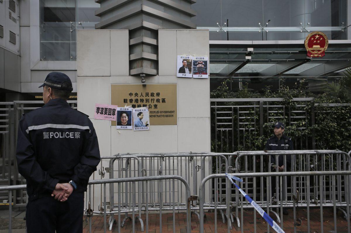 Police officers stand guard after protesters stick photos of missing booksellers during a protest outside the Liaison of the Central People's Government in Hong Kong, on Jan. 3, 2016. Hong Kong pro-democracy lawmakers say they'll press the government for answers after a fifth employee of a publisher specializing in books critical of China's ruling communists went missing. (Vincent Yu/AP Photo)