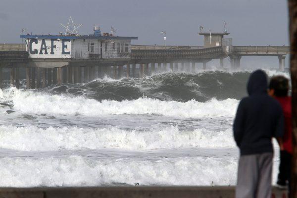 People watch as large surf rolls to the beach past the Ocean Beach Pier which was closed because of the high surf after strong storms in San Diego on Jan. 7. (Bill Wechter/AFP/Getty Images)