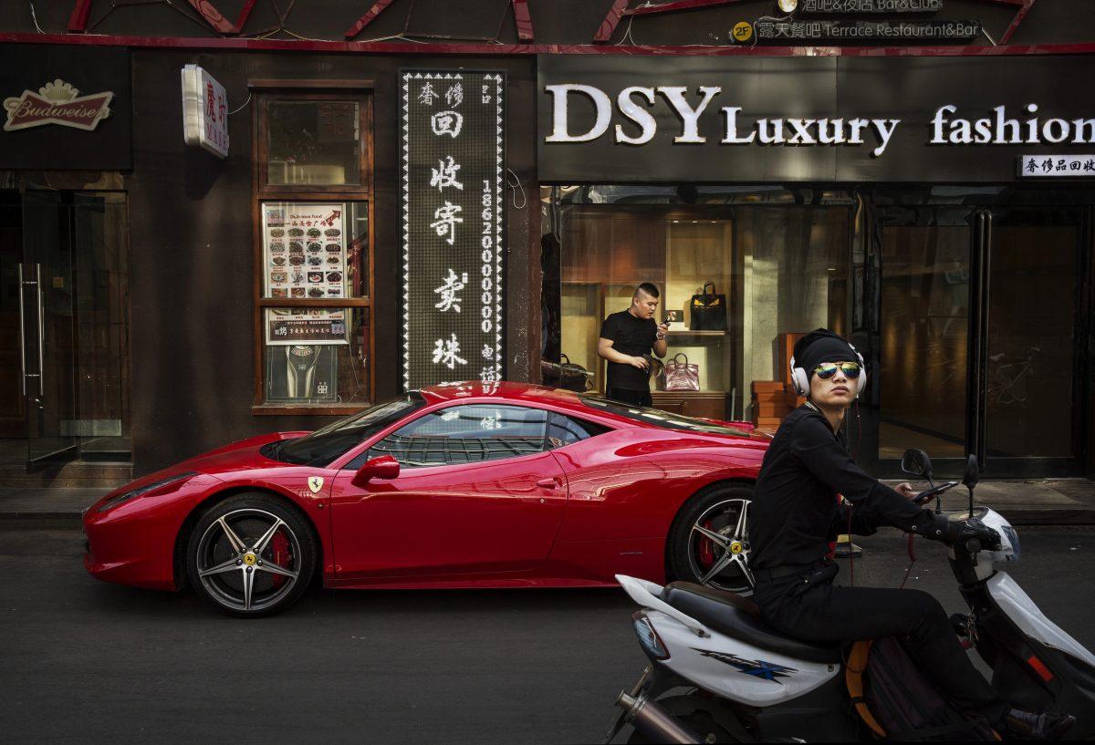 A Chinese man uses his phone next to his Ferrari in an upscale shopping district in Beijing on May 29, 2015. (Kevin Frayer/Getty Images)