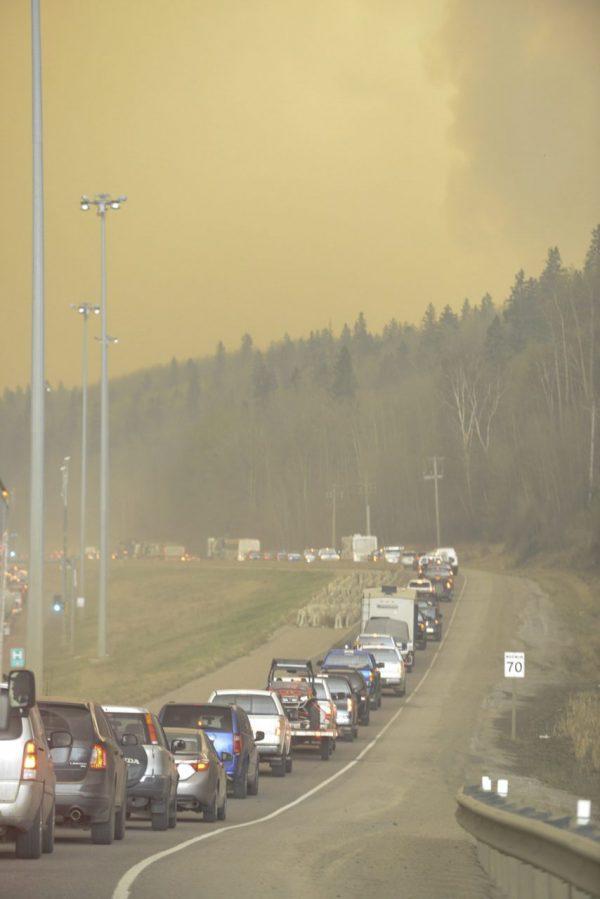 Smoke fills the air as people drive on a road in Fort McMurray, Alberta, Tuesday, May 3, 2016. At least half of a northern Alberta city was ordered evacuated Tuesday as a wildfire whipped by winds engulfed homes and sent ash raining down on residents. (Greg Halinda/The Canadian Press via AP)