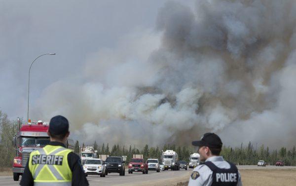 Police watch a convoy of cars and trucks pass a wildfire as they are evacuated from Fort McMurray, Alberta, on May 7, 2016. (Jonathan Hayward /The Canadian Press via AP)