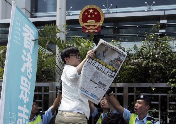 A member of the pro-democracy group Demosisto, Oscar Lai, holds the newspaper with a picture of Hong Kong bookseller Lam Wing-Kee in front of the Hong Kong liaison office, on June 17, 2016. (AP Photo/Kin Cheung)