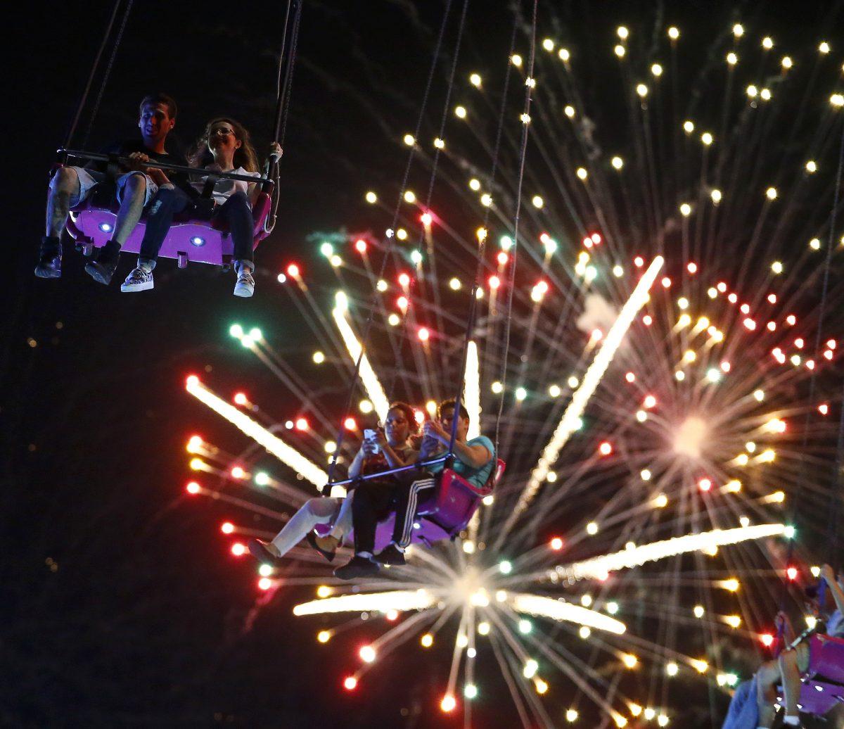 People ride the Sky Flyer at State Fair Meadowlands carnival as fireworks explode, in East Rutherford, N.J., on July 3, 2013. (Julio Cortez/AP Photo)