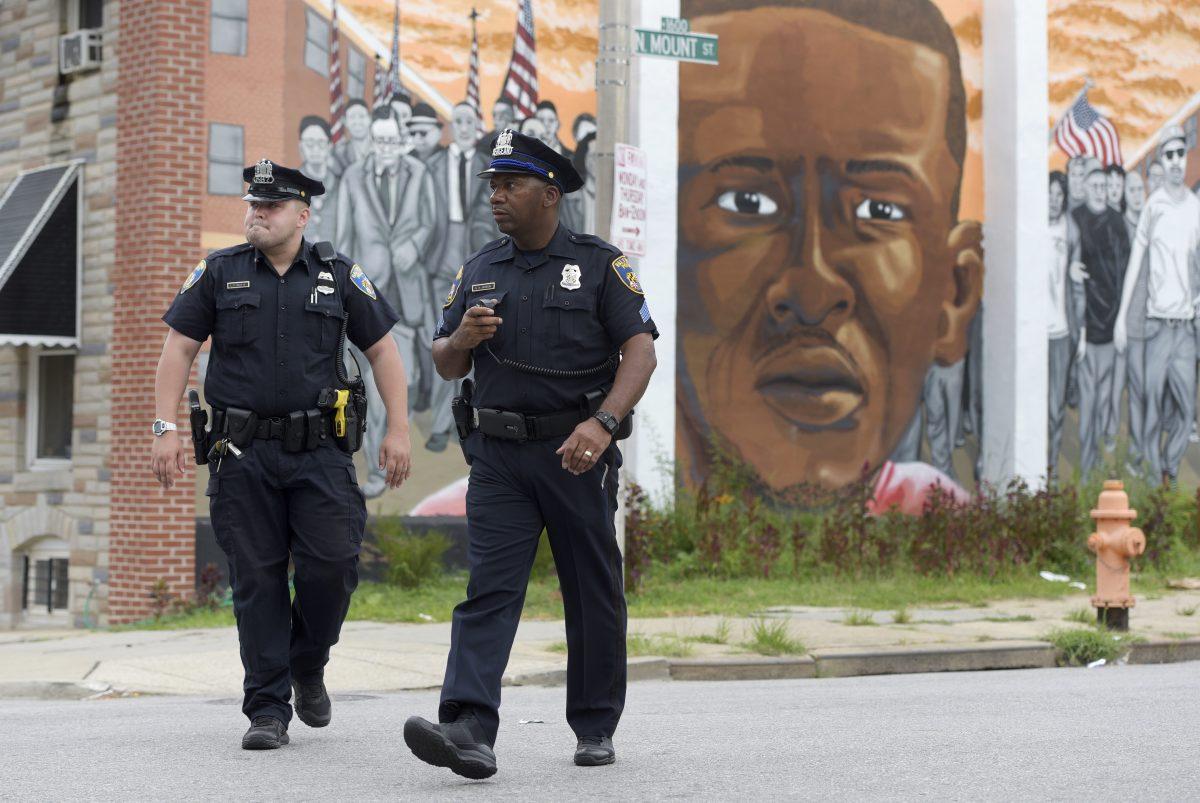 Baltimore police walk near a mural depicting Freddie Gray after prosecutors dropped remaining charges against the three Baltimore police officers who were still awaiting trial in Gray’ death, in Baltimore on July 27, 2016. (Steve Ruark/AP Photo)