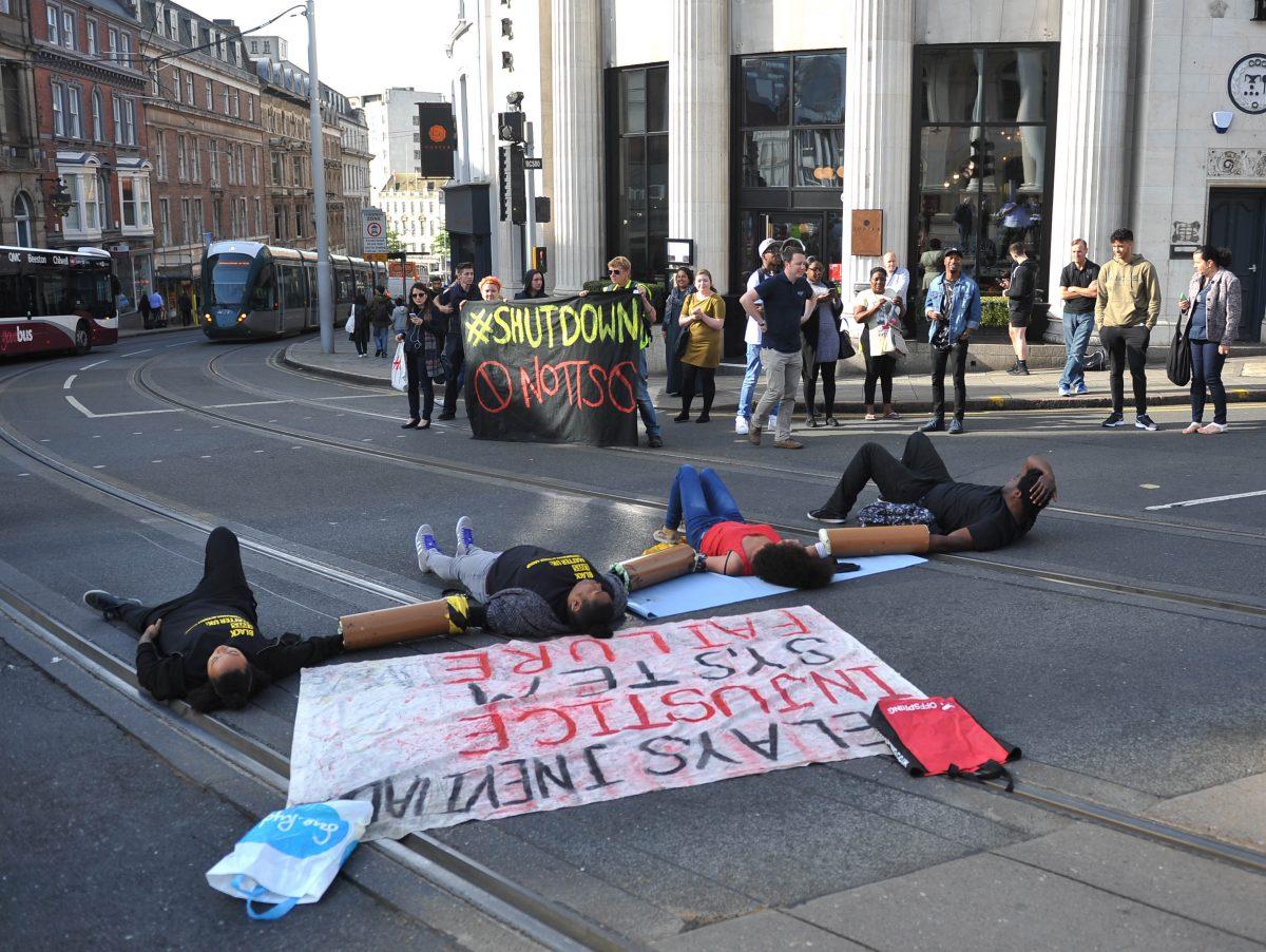 Activists lie on the road outside Nottingham Theatre Royal as they attempt to shut down part of the city centre tram and bus network in Nottingham, England, on Aug. 5, 2016. (Edward Smith/PA via AP)