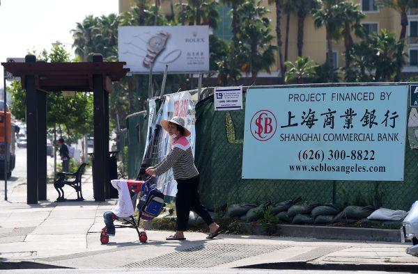 A woman pushes a stroller past a banner at a construction site project financed by the Shanghai Commercial Bank, in San Gabriel, Calif., on May 17, 2016. A massive surge in Chinese buying of both commercial U.S. real estate and residential property last year took their five-year investment total to more than $110 billion, according to a study from the Asia Society and Rosen Consulting Group, as Chinese nationals became the largest foreign buyers of U.S. homes. (Frederic J. Brown/AFP/Getty Images)