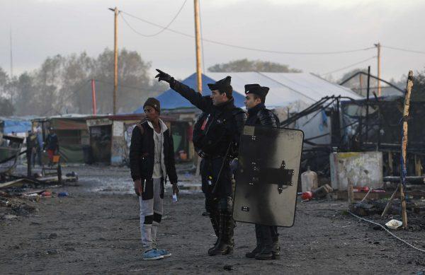 French police officers direct a migrant in the remains of the makeshift migrant camp known as "the jungle" near Calais, northern France, Oct. 27, 2016. (AP Photo/Emilio Morenatti)