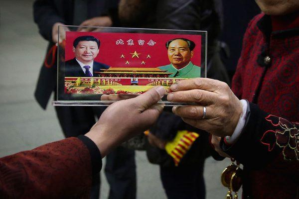 A Chinese street vendor displays a souvenir with pictures of Chinese President Xi Jinping (Left) and late Chinese Communist Party Chairman Mao Zedong (Right) outside the Great Hall of the People, in Beijing, China, on Nov. 12, 2013. (Feng Li/Getty Images)