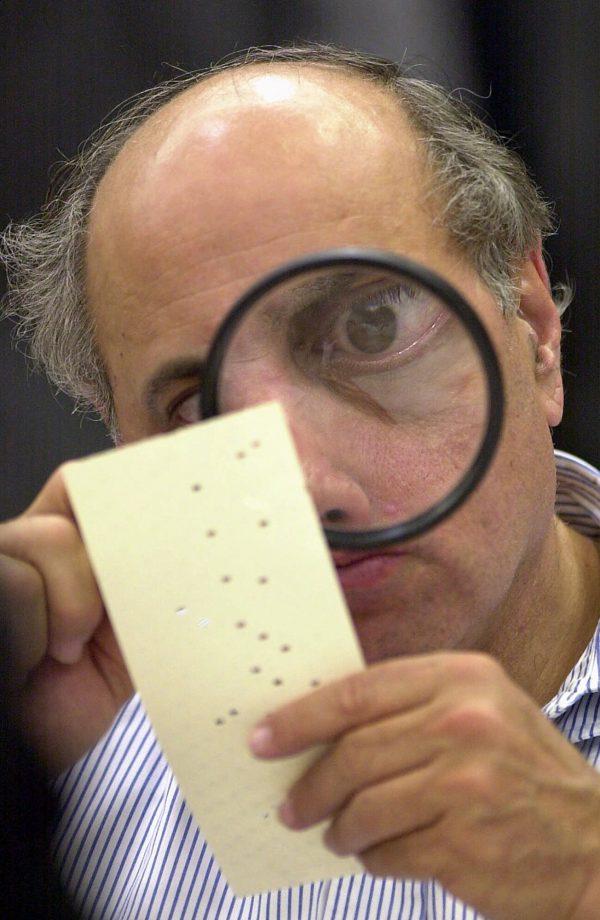 Broward County canvassing board member Judge Robert Rosenberg uses a magnifying glass on Nov. 24, 2000, to examine a disputed ballot at the County Courthouse in Fort Lauderdale, Fla. (AP Photo/Alan Diaz, File)
