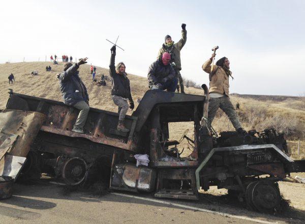 Protesters against the Dakota Access oil pipeline stand on a burned-out truck near Cannon Ball, N.D., that they removed from a long-closed bridge a day earlier on a state highway near their camp, in this file photo. (James MacPherson/File/AP Photo)