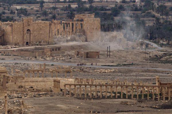 Russian soldiers stand on a road as smoke rises from a controlled land mine detonation by Russian experts inside the ancient town of Palmyra, Syria, on April 14, 2016. (Hassan Ammar/AP Photo)