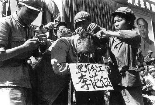 Communist Party cadres hang a placard on the neck of a Chinese man. The words on the placard state the man's name and accuse him of being a member of the "black class" (Public Domain)