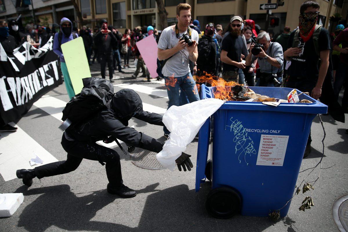 An Antifa extremist pushes a burning recycling bin at Trump supporters during a free speech rally in Berkeley, Calif., on April 15. (Elijah Nouvelage/Getty Images)