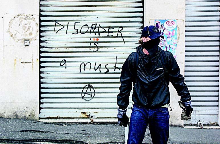 A far-left protester holds rocks in front of graffiti reading “Disorder is a must” with an anarchist symbol beneath it, during the G-8 summit in Genoa, Italy, in 2001. (SEAN GALLUP/GETTY IMAGES)
