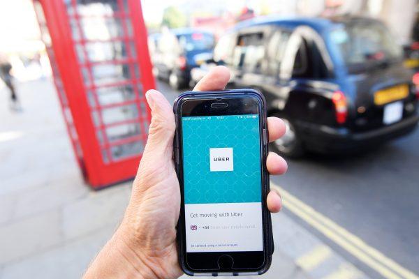 A photo illustration shows a London taxi passing as the Uber app logo is displayed on a mobile telephone, as it is held up for a posed photograph in central London on Sept. 22, 2017. (Toby Melville/Reuters)