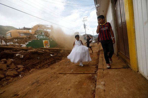 A girl in a communion dress walks past a demolition machine tearing down a house damaged by an earthquake, in Tecomatlan, Mexico September 23, 2017. (Reuters/Edgard Garrido)