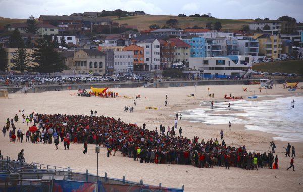 Surf lifesavers can be seen behind protesters participating in a national Day of Action against the Indian mining company Adani's planned coal mine project in north-east Australia, at Sydney's Bondi Beach in Australia, October 7, 2017. (Reuters/David Gray)
