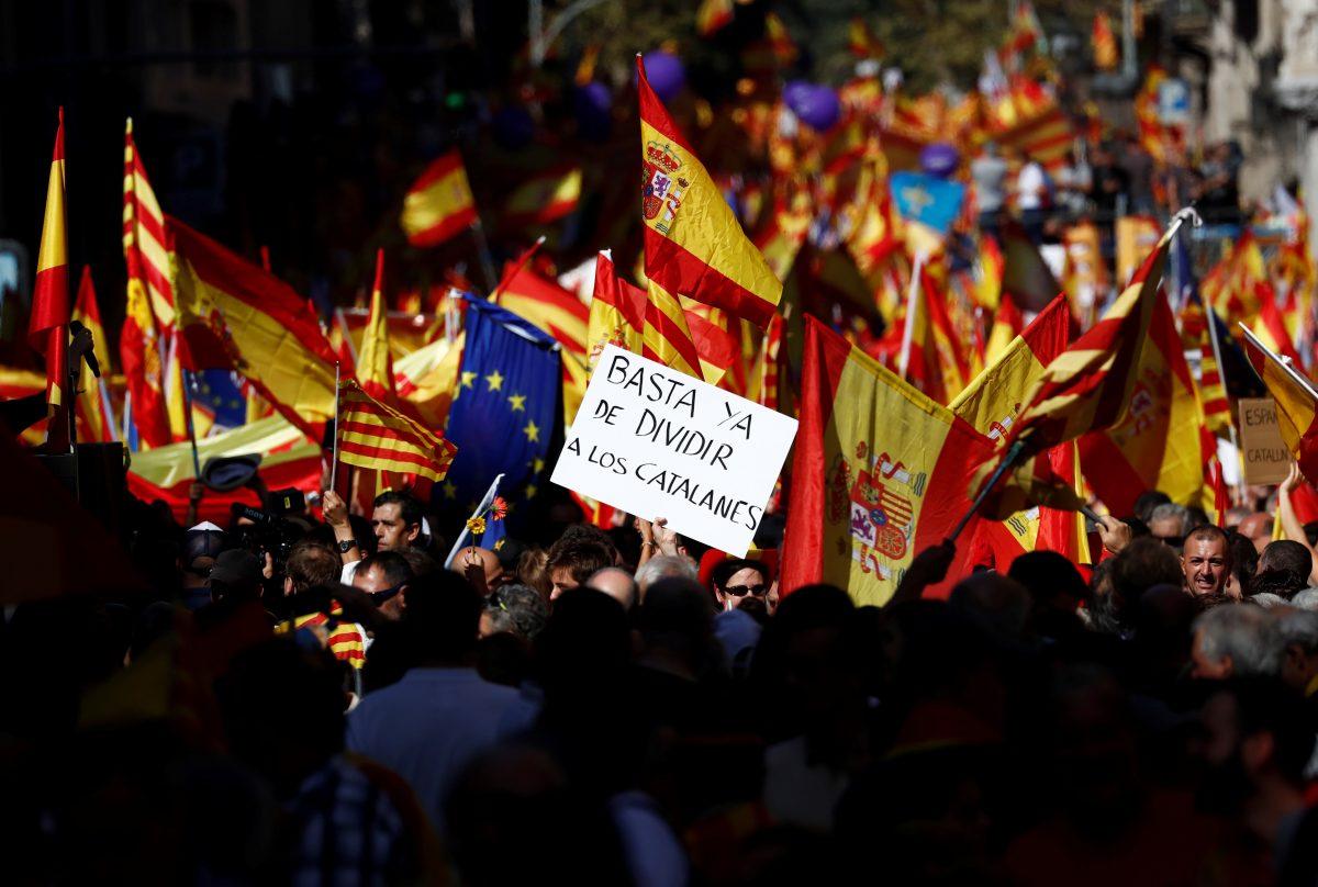 A sign reads "Stop dividing Catalans now" in Spanish as a pro-union demonstration organized by the Catalan Civil Society organization makes its way through the streets of Barcelona, Spain on Oct. 8, 2017. (REUTERS/Juan Medina)
