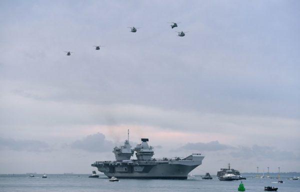 Wildcat and Merlin helicopters fly above the 65,000-ton British aircraft carrier HMS Queen Elizabeth as tugboats manoeuvre it into Portsmouth Harbour in Portsmouth, southern England, on Aug. 16, 2017. (Ben Stansall/AFP/Getty Images)