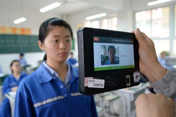 Facial recognition system is being rapidly introduced across China. Stock photo shows a teacher uses a machine which employs both fingerprint and facial recognition technology to check the identification of a student before a simulated college entrance exam in Hebei province on June 6, 2017. (STR/AFP/Getty Images)