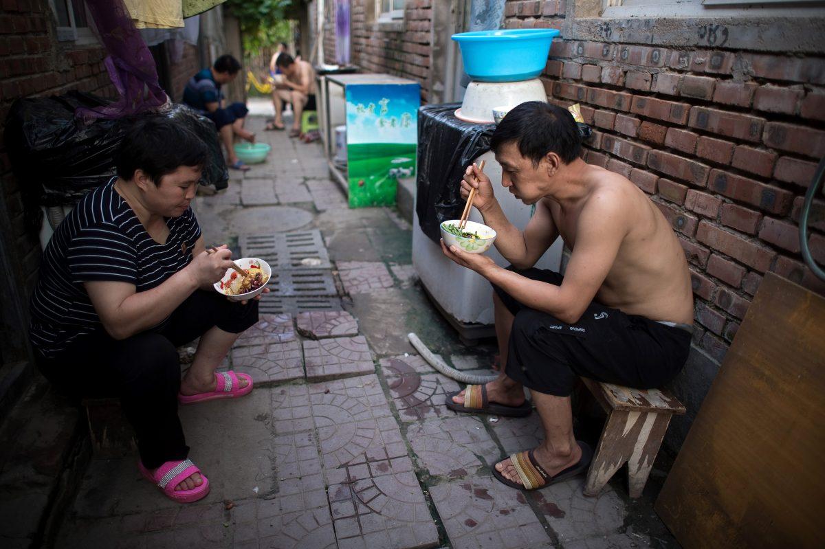People eat dinner outside their rooms on a street in a migrant village on the outskirts of Beijing on Aug. 17, 2017. (Nicolas Asfouri/AFP/Getty Images)