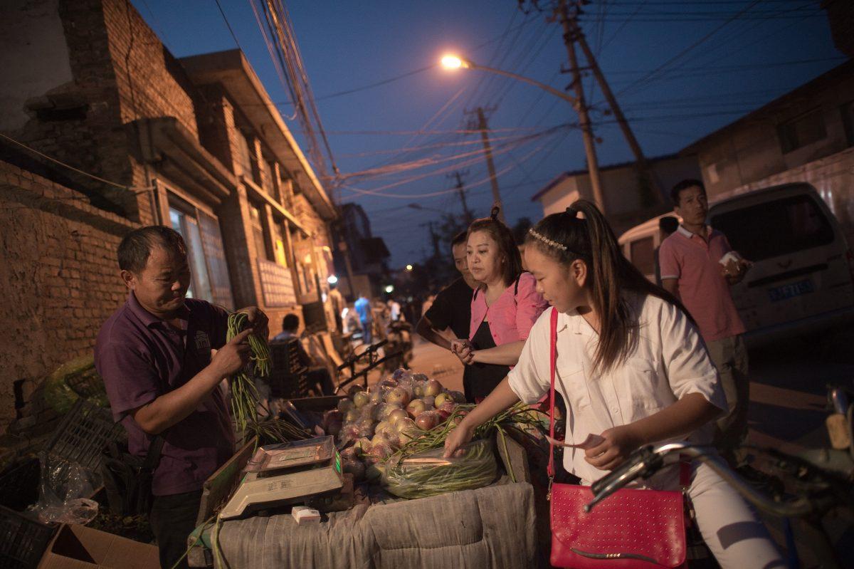 People buy vegetables at a stand in a migrant village on the outskirts of Beijing on Sept. 7, 2017. Surrounded by the sleek hi-tech campuses and luxury condominiums of "Beijing's Silicon Valley," migrants from the countryside recreate village life, cooking in outdoor communal areas, playing cards and showering in the street. (Nicolas Asfouri/AFP/Getty Images)