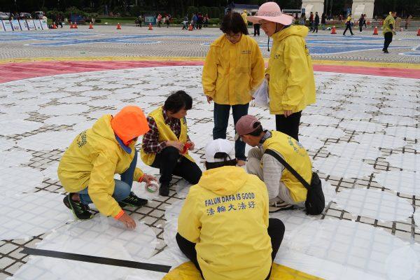Chen Hsin-lin (second from left) tapes a colored mat onto the floor at Liberty Square on Nov. 24, 2017. (Frank Fang/The Epoch Times)