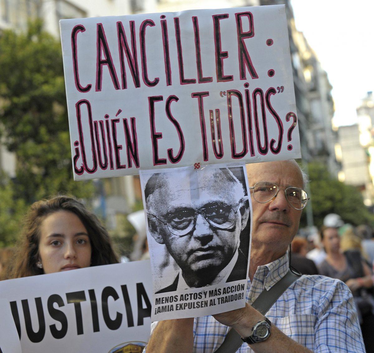 A man holds a placard with the picture of Argentinian Foreign Minister Hector Timerman and another one that reads "Foreign Minister: Who Is Your God" during a rally in front of the headquarters of the AMIA (Argentine Israelite Mutual Association), in Buenos Aires on January 21, 2015, to protest against the death of Argentine public prosecutor Alberto Nisman, who was found shot dead earlier, just days after accusing former President Cristina Fernández de Kirchner of obstructing a probe into a 1994 Jewish center bombing that killed 85 peiople and injured another 300. Nisman, 51, who was just hours away from testifying at a congressional hearing, was found dead overnight in his apartment in the trendy Puerto Madero neighbourhood of the capital. "I can confirm that a 22-caliber handgun was found beside the body," prosecutor Viviana Fein said. The nation's top security official said Nisman appears to have committed suicide. (Alejandro Pagni/AFP/Getty Images)
