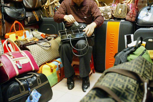 A shop keeper polishes a fake Prada bag while seated among other imitation goods in Guangzhou City, China, on November 18 2004. (Laurent Fievet/AFP/Getty Images)