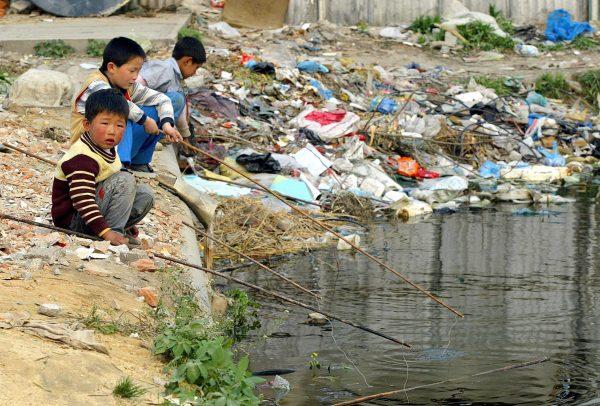 Local children fish in a backwater surrounded by discarded rubbish in Shanghai, on June 14, 2004. (Liu Jin/AFP/Getty Images)