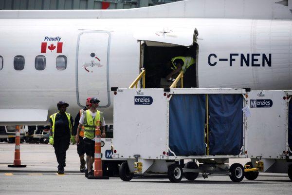 Baggage handlers remove luggage from a WestJet aircraft on July, 28, 2017. (The Canadian Press/Christopher Katsarov)