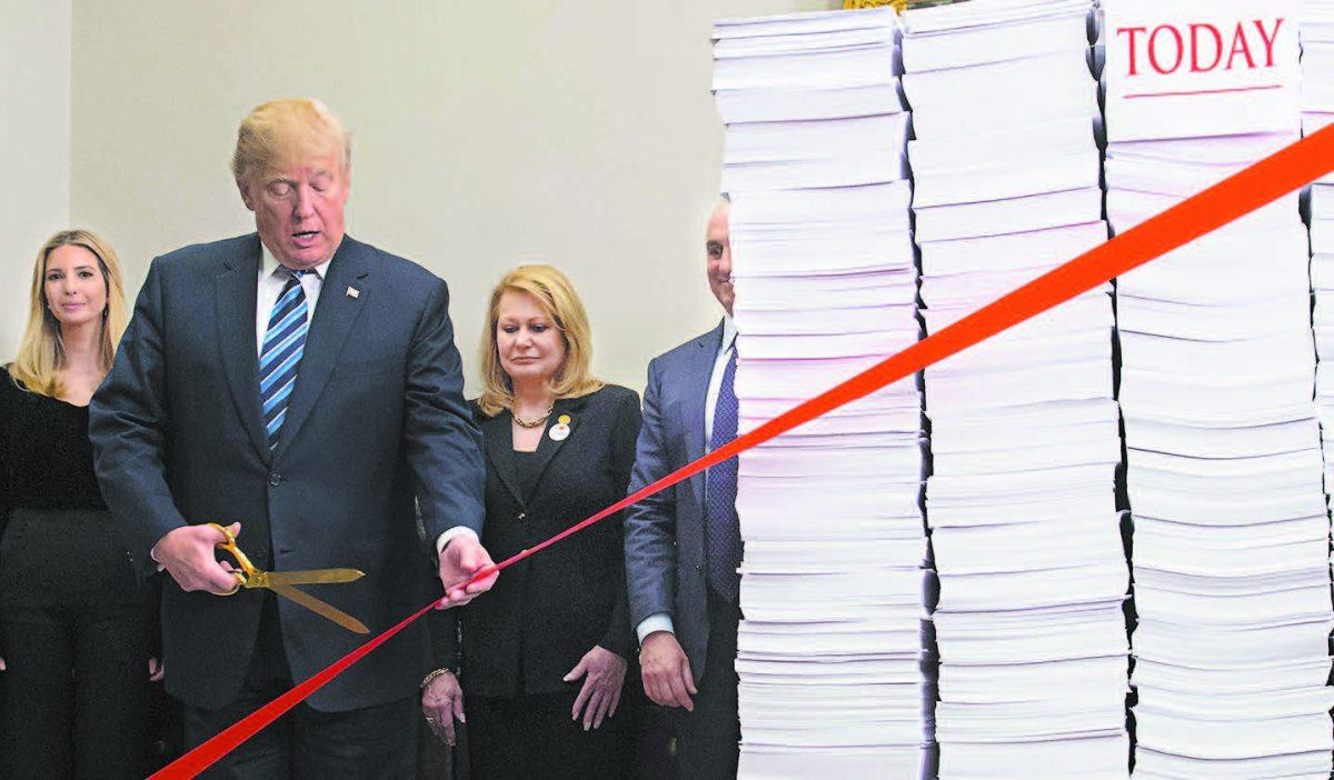 President Donald Trump cuts a red tape tied between two stacks of papers representing the government regulations of 1960 and the regulations of today after he spoke about his administration’s efforts in deregulation, at the White House on Dec. 14, 2017. (SAUL LOEB/AFP/GETTY IMAGES)