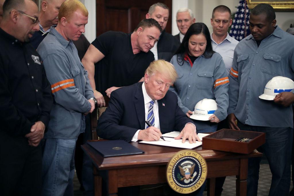 Surrounded by steel and aluminum workers, U.S. President Donald Trump signs a ‘Section 232 Proclamation’ on steel imports during a ceremony in the Roosevelt Room at the White House in Washington, on March 8, 2018. (Chip Somodevilla/Getty Images)