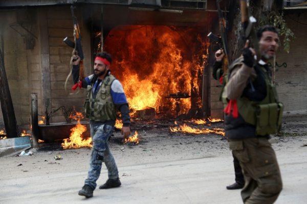 Turkish-backed Syrian rebels walk past a burning shop in the city of Afrin in northern Syria on March 18, 2018. (Nazeer Al-Khatib/AFP/Getty Images)