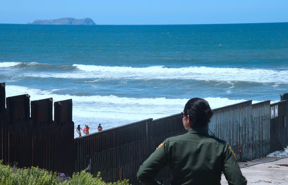 A US Customs and Border Protection agent watches from near the end of the border structure which runs into the Pacific Ocean in San Diego, California, as people visit the beach in La Playa, Mexico, on April 17, 2018, a day after California rejected plans by the federal government for National Guard troops on the border. (FREDERIC J. BROWN/AFP/Getty Images)
