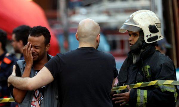 Firefighter officers comfort a man near the site where the building collapsed. (Reuters/Leonardo Benassatto)