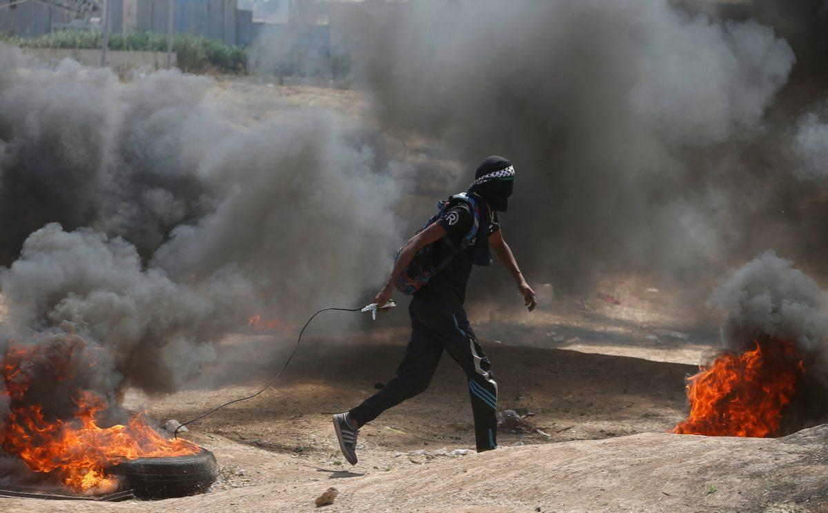 A Palestinian demonstrator drags a burning tire during a protest against U.S. embassy move to Jerusalem and ahead of the 70th anniversary of Nakba, at the Israel-Gaza border, east of Gaza City May 14, 2018. REUTERS/Mohammed Salem