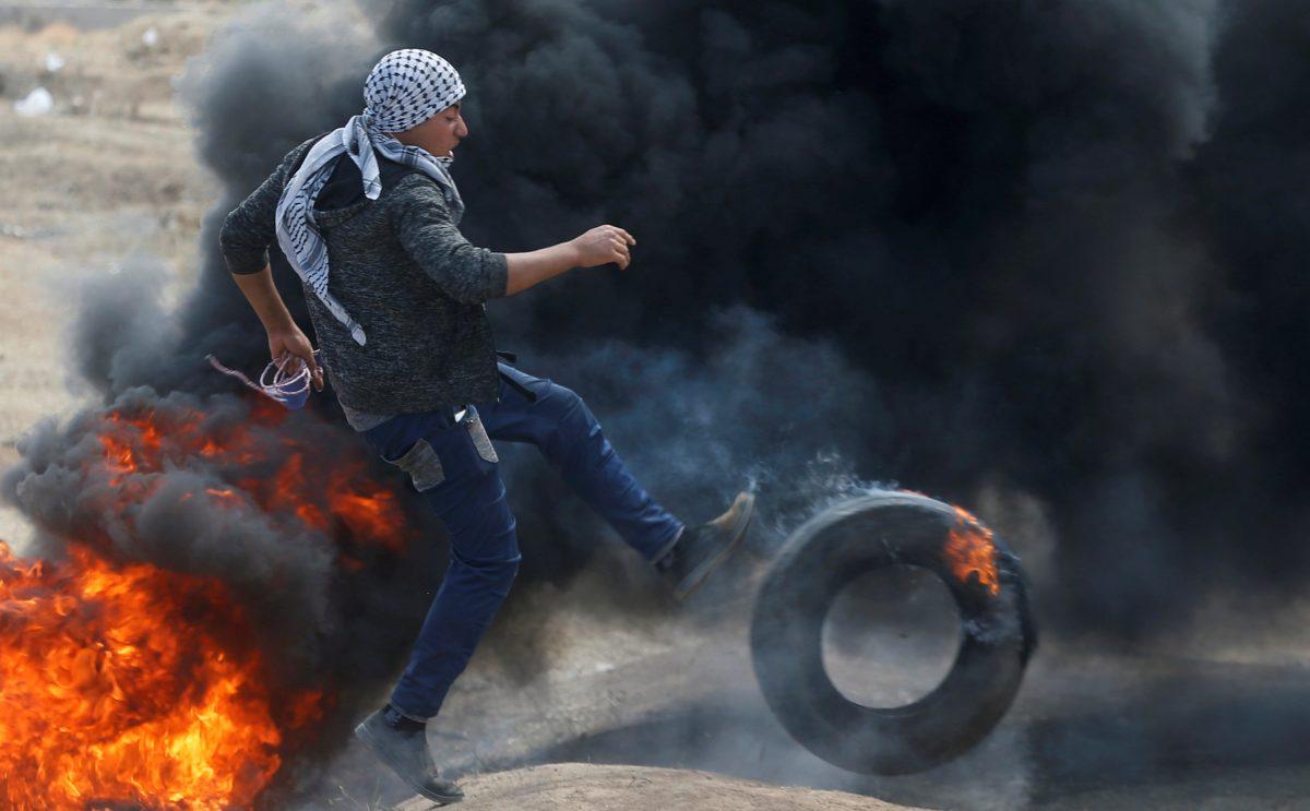 A Palestinian demonstrator kicks a burning tire during a protest against U.S. embassy move to Jerusalem and ahead of the 70th anniversary of Nakba, at the Israel-Gaza border, east of Gaza City May 14, 2018. REUTERS/Mohammed Salem