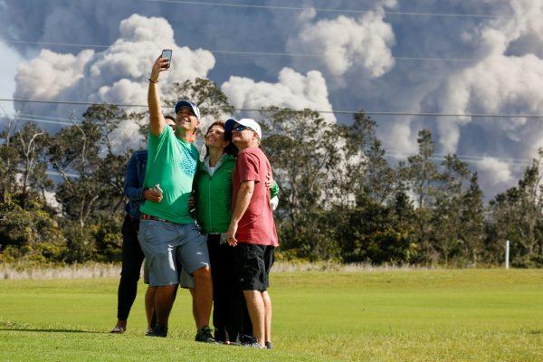Sean Bezecny, 46, of Houston, Texas, takes a photo with his family and friends as ash erupts from the Halemaumau Crater near the community of Volcano during ongoing eruptions of the Kilauea Volcano in Hawaii, U.S., May 19, 2018. (Reuters/Terray Sylvester)