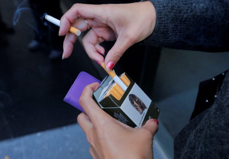 FILE PHOTO: A photo illustration shows a smoker with a pack of cigarettes featuring restrictive tobacco packaging outside a Sydney office building in Australia, May 5, 2017. (Reuters/Jason Reed)