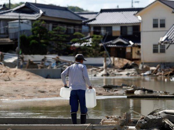 A local resident carries waters near submerged and destroyed houses in a flooded area in Mabi town in Kurashiki, Okayama Prefecture, Japan, July 9, 2018. (Reuters/Issei Kato)