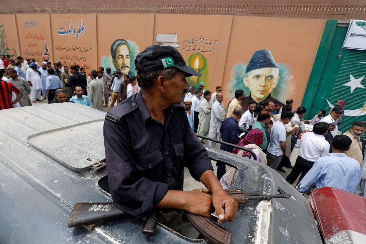 A police officer guards, where electoral workers stand in line to collect election materials ahead of general election in Karachi, Pakistan July 24, 2018. (Reuters/Akhtar Soomro)