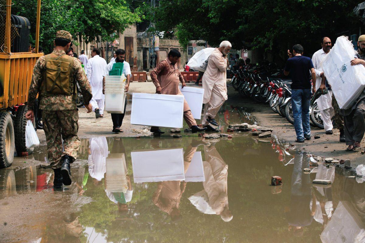 Electoral workers are seen reflected in a puddle of sewage as they carry election materials after collecting them at a distribution point, ahead of general election in Lahore, Pakistan July 24, 2018. (Reuters/Mohsin Raza)