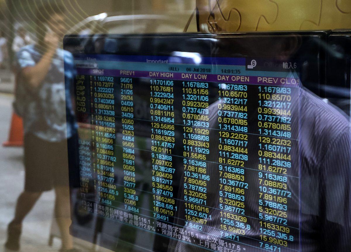 Pedestrians are reflected in the window of a brokerage with a screen showing currency exchange rates in Hong Kong on July 6, 2018. The yuan has dropped in value, following the imposition of U.S. tariffs on Chinese goods. (VIVEK PRAKASH/AFP/Getty Images)